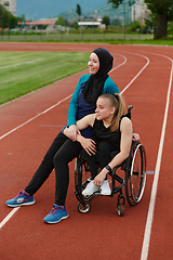 Image showing A Muslim woman wearing a burqa resting with a woman with disability after a hard training session on the marathon course