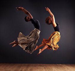Image showing Synchronisity. Two contemporary dancers performing a synchronized leap in front of a dark background.