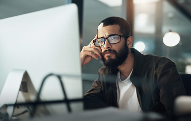 Image showing The later it gets the deeper he goes. Shot of a young businessman using a computer during a late night in a modern office.