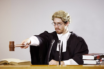 Image showing Silence. Serious young judge sitting in the courtroom with a stern facial expression while holding out a gavel.