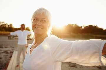 Image showing Every day is a yoga day. Shot of a mature woman doing yoga on the beach with her husband in the background.