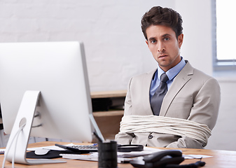 Image showing Hes always stuck to his desk. A handsome young businessman tied up and sitting at his desk.