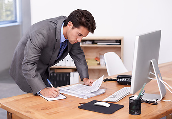 Image showing A lot of things on the go at once. A handsome businessman multitasking at his desk.