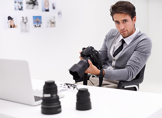 Image showing Young and creative photographer. Portrait of a photographer sitting at a desk in his office holding a camera.