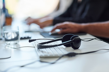 Image showing Get the assistance you need. Shot of a set of headsets lying on a desk with workers sitting in the background.