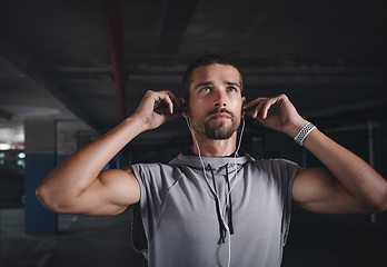 Image showing Music is my motivation. Shot of a handsome young sportsman listening to music on his earphones while exercising inside a parking lot.