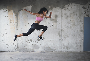 Image showing Springing back into action. Full length shot of an athletic young sportswoman jumping in the air against a wall outdoors.