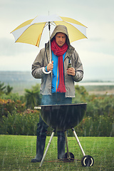 Image showing Real men bbq anytime. Shot of a man barbecuing in the rain.