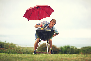 Image showing The rain wont stop my barbecue. Shot of a man trying to barbeque in the rain.