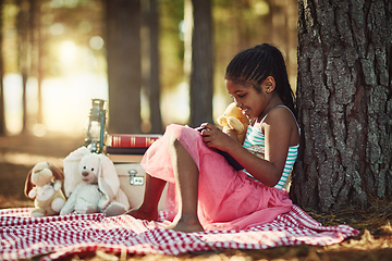 Image showing Story time with her favourite little teddy. Shot of a little girl reading a book with her toys in the woods.