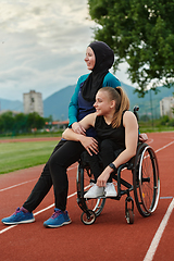 Image showing A Muslim woman wearing a burqa resting with a woman with disability after a hard training session on the marathon course