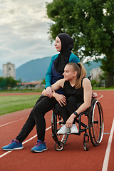 Image showing A Muslim woman wearing a burqa resting with a woman with disability after a hard training session on the marathon course