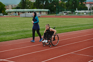 Image showing A Muslim woman in a burqa running together with a woman in a wheelchair on the marathon course, preparing for future competitions.