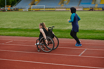 Image showing A Muslim woman in a burqa running together with a woman in a wheelchair on the marathon course, preparing for future competitions.