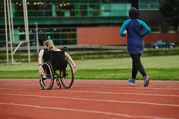 Image showing A Muslim woman in a burqa running together with a woman in a wheelchair on the marathon course, preparing for future competitions.