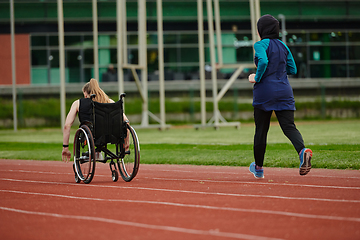 Image showing A Muslim woman in a burqa running together with a woman in a wheelchair on the marathon course, preparing for future competitions.