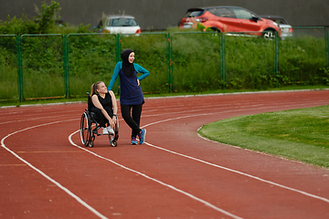 Image showing A Muslim woman wearing a burqa resting with a woman with disability after a hard training session on the marathon course