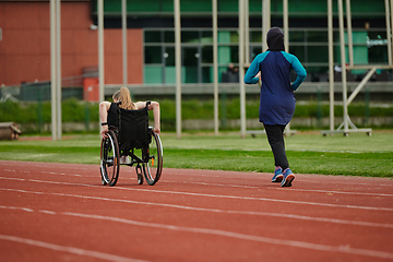 Image showing A Muslim woman in a burqa running together with a woman in a wheelchair on the marathon course, preparing for future competitions.