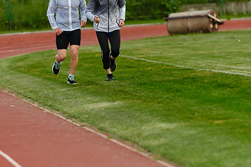 Image showing An inspiring and active elderly couple showcase their dedication to fitness as they running together on a lush green field, captured in a close-up shot of their legs in motion.