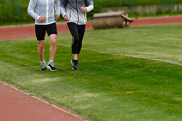 Image showing An inspiring and active elderly couple showcase their dedication to fitness as they running together on a lush green field, captured in a close-up shot of their legs in motion.