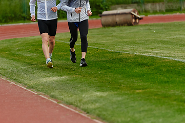 Image showing An inspiring and active elderly couple showcase their dedication to fitness as they running together on a lush green field, captured in a close-up shot of their legs in motion.