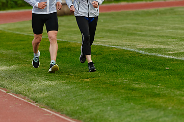 Image showing An inspiring and active elderly couple showcase their dedication to fitness as they running together on a lush green field, captured in a close-up shot of their legs in motion.