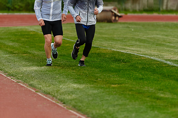 Image showing An inspiring and active elderly couple showcase their dedication to fitness as they running together on a lush green field, captured in a close-up shot of their legs in motion.