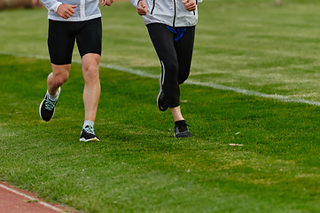 Image showing An inspiring and active elderly couple showcase their dedication to fitness as they running together on a lush green field, captured in a close-up shot of their legs in motion.