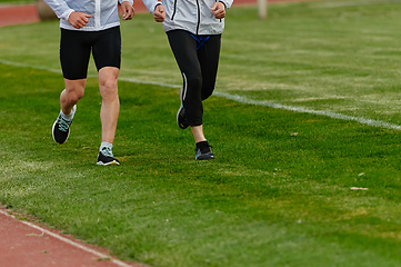 Image showing An inspiring and active elderly couple showcase their dedication to fitness as they running together on a lush green field, captured in a close-up shot of their legs in motion.