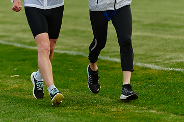 Image showing An inspiring and active elderly couple showcase their dedication to fitness as they running together on a lush green field, captured in a close-up shot of their legs in motion.