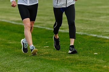 Image showing An inspiring and active elderly couple showcase their dedication to fitness as they running together on a lush green field, captured in a close-up shot of their legs in motion.