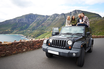 Image showing Stopping to experience the breathtaking view. Shot of a group of friends relaxing on the roof of their truck with a mountainous background.