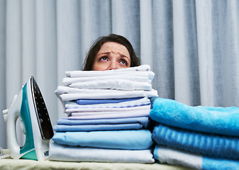 Image showing Too much to do, too little time. Shot of an anxious looking young woman behind a pile of laundry on an ironing board.