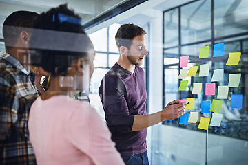 Image showing Dividing tasks between the team. Cropped shot of a team of designers brainstorming with notes on a glass wall in an office.