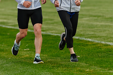 Image showing An inspiring and active elderly couple showcase their dedication to fitness as they running together on a lush green field, captured in a close-up shot of their legs in motion.