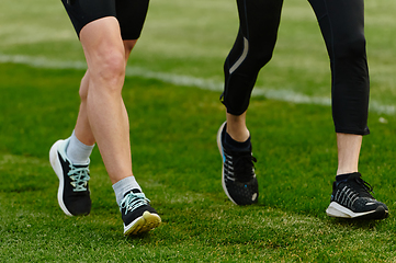 Image showing An inspiring and active elderly couple showcase their dedication to fitness as they running together on a lush green field, captured in a close-up shot of their legs in motion.