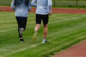 Image showing An inspiring and active elderly couple showcase their dedication to fitness as they running together on a lush green field, captured in a close-up shot of their legs in motion.