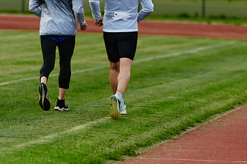 Image showing An inspiring and active elderly couple showcase their dedication to fitness as they running together on a lush green field, captured in a close-up shot of their legs in motion.