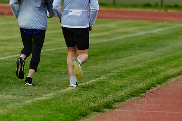 Image showing An inspiring and active elderly couple showcase their dedication to fitness as they running together on a lush green field, captured in a close-up shot of their legs in motion.