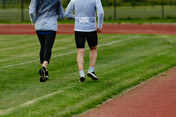 Image showing An inspiring and active elderly couple showcase their dedication to fitness as they running together on a lush green field, captured in a close-up shot of their legs in motion.