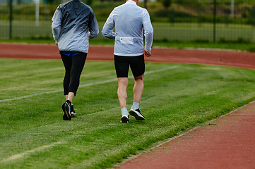 Image showing An inspiring and active elderly couple showcase their dedication to fitness as they running together on a lush green field, captured in a close-up shot of their legs in motion.