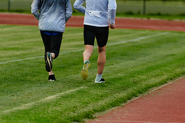 Image showing An inspiring and active elderly couple showcase their dedication to fitness as they running together on a lush green field, captured in a close-up shot of their legs in motion.