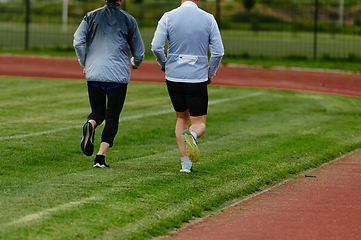 Image showing An inspiring and active elderly couple showcase their dedication to fitness as they running together on a lush green field, captured in a close-up shot of their legs in motion.