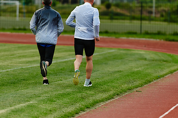 Image showing An inspiring and active elderly couple showcase their dedication to fitness as they running together on a lush green field, captured in a close-up shot of their legs in motion.