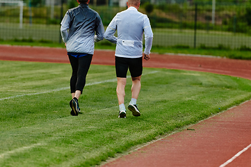 Image showing An inspiring and active elderly couple showcase their dedication to fitness as they running together on a lush green field, captured in a close-up shot of their legs in motion.