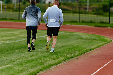 Image showing An inspiring and active elderly couple showcase their dedication to fitness as they running together on a lush green field, captured in a close-up shot of their legs in motion.