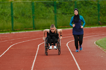 Image showing A Muslim woman in a burqa running together with a woman in a wheelchair on the marathon course, preparing for future competitions.