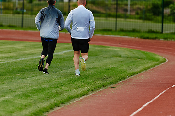 Image showing An inspiring and active elderly couple showcase their dedication to fitness as they running together on a lush green field, captured in a close-up shot of their legs in motion.