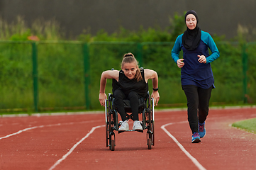 Image showing A Muslim woman in a burqa running together with a woman in a wheelchair on the marathon course, preparing for future competitions.