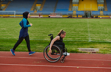 Image showing A Muslim woman in a burqa running together with a woman in a wheelchair on the marathon course, preparing for future competitions.